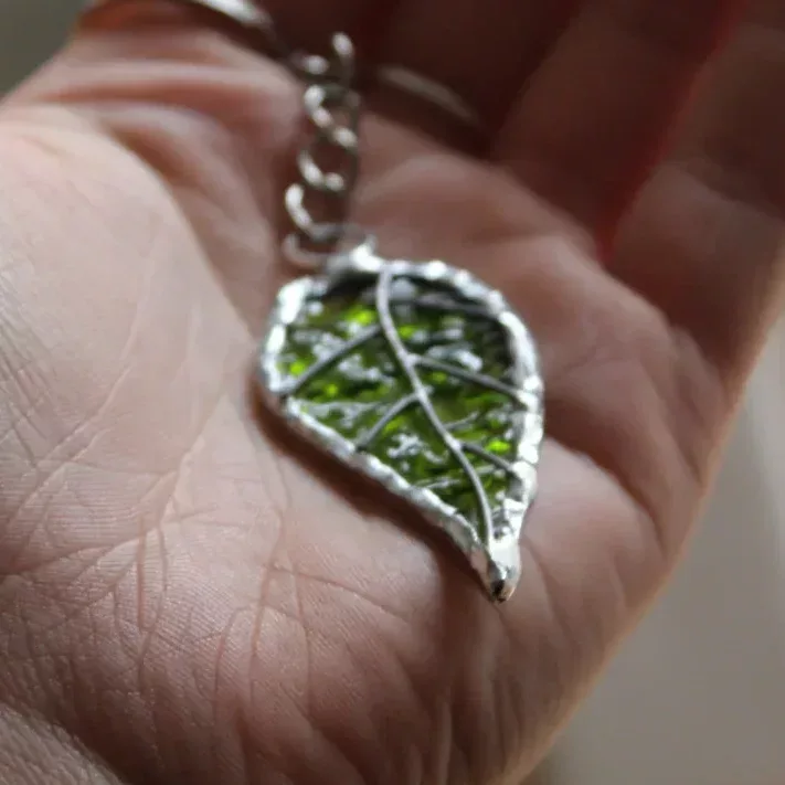 Porte-clés feuille en vitrail vert texturé et métal argenté tenu dans une main.