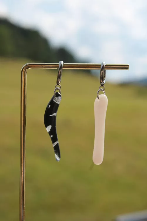 Boucles d'oreilles asymétriques, l'une noire courbée et l'autre blanche droite, suspendues sur un support doré.