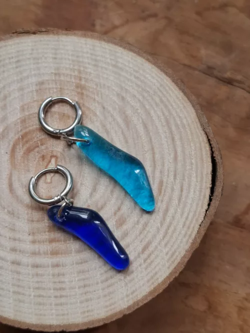 Boucles d'oreilles pendantes en verre recyclé bleu turquoise et bleu nuit posées sur un disque en bois.
