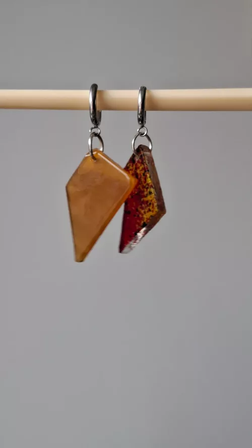 Boucles d’oreilles asymétriques en verre jaune ocre et rouge moucheté suspendues sur une tige en bois.