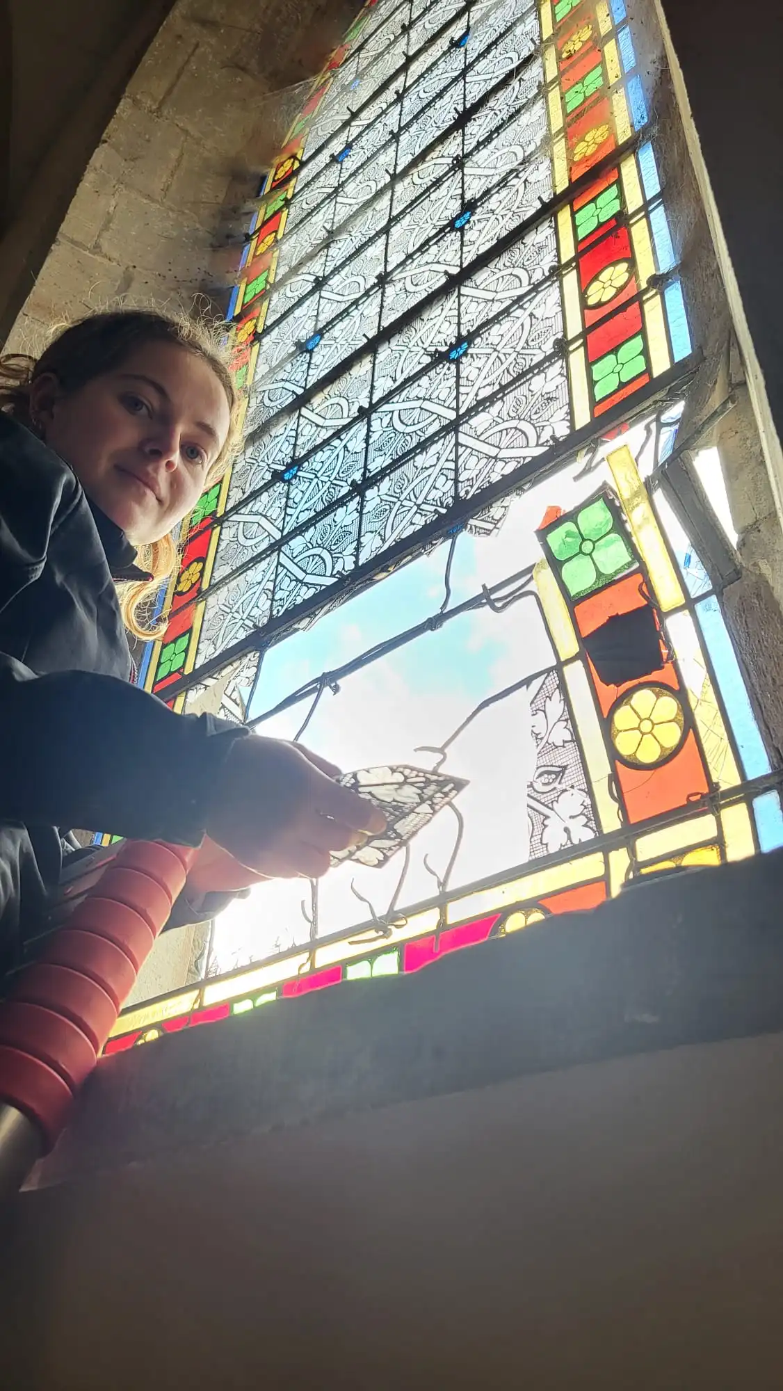 Restauration in situ : intervention de la vitrailliste sur le panneau endommagé